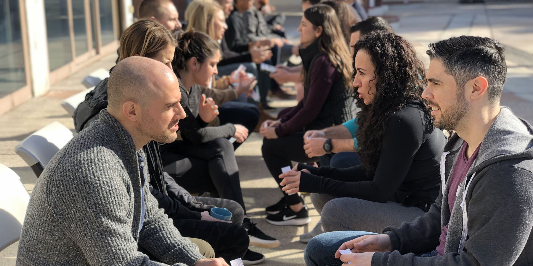 Leaders sitting in pairs outdoors, deep in one-to-one conversation at a retreat.