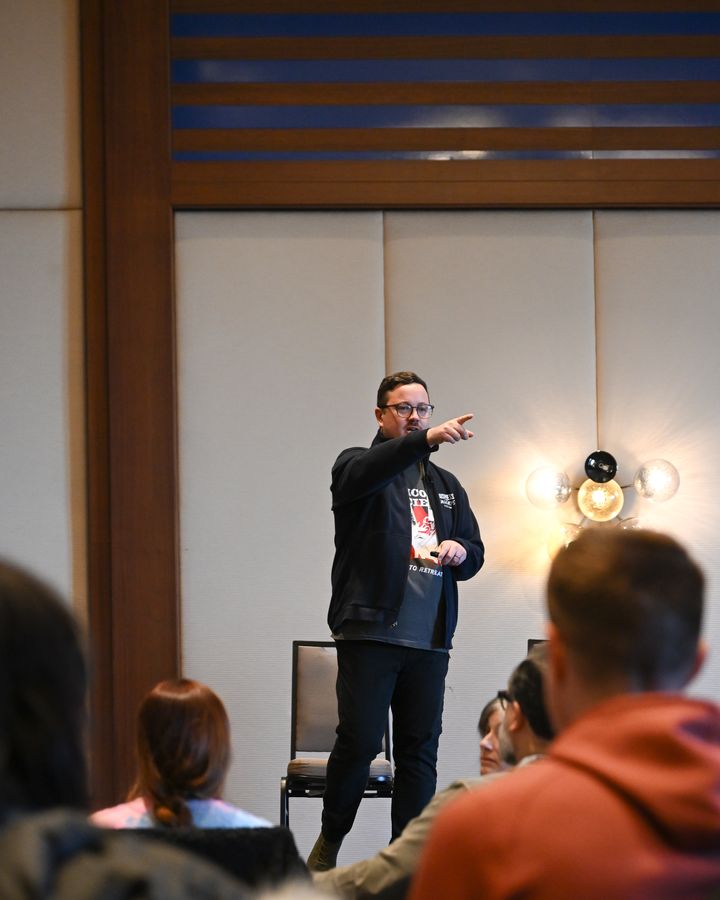 Michael mid-talk, gesturing to a seated audience.