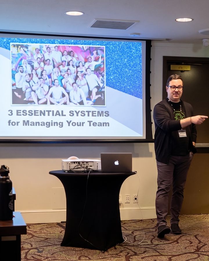 Michael presenting beside a slide reading Three Essential Systems for Managing Your Team.
